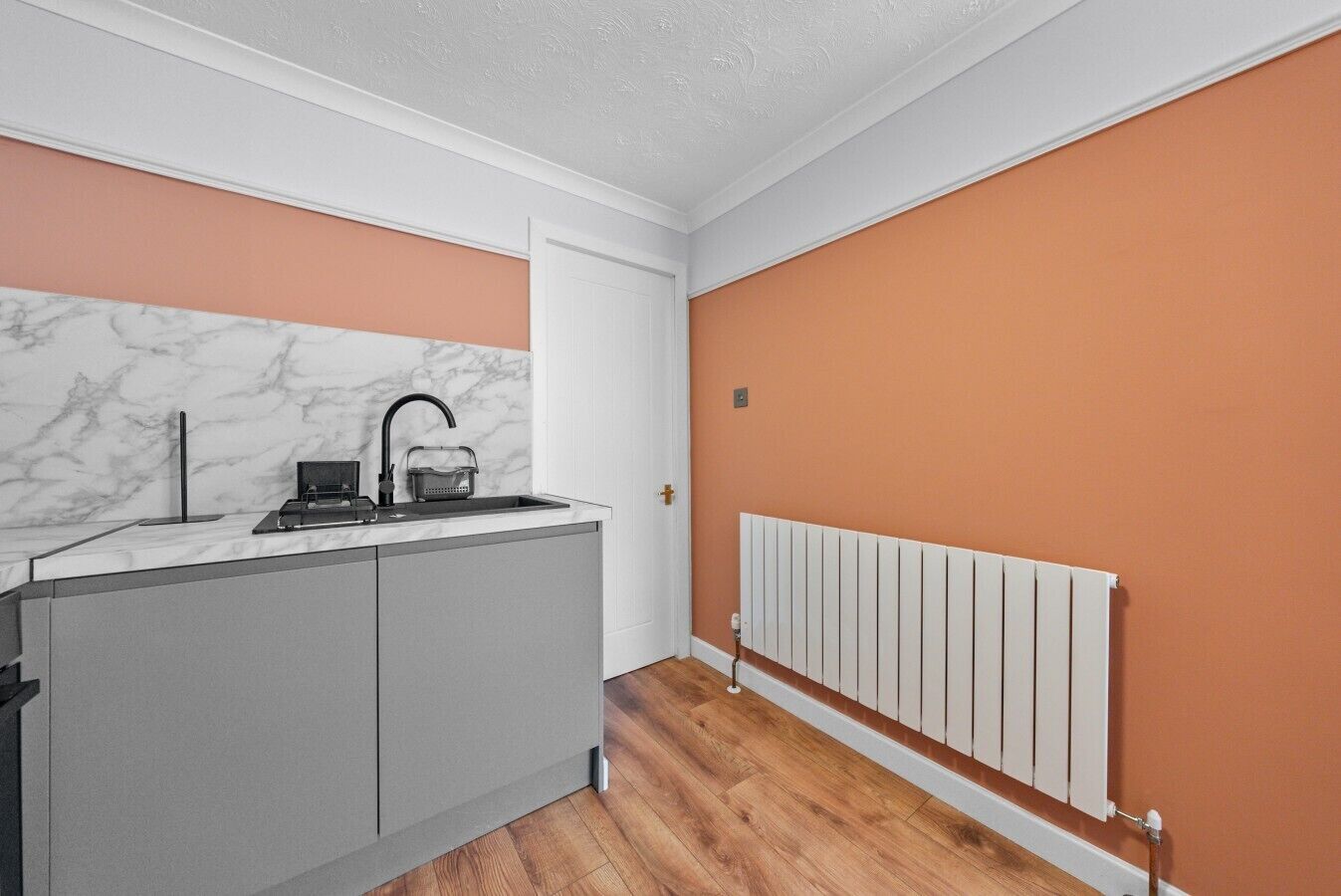 A compact kitchen with a marble backsplash, a built-in oven, and a white radiator.