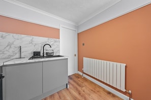 A compact kitchen with a marble backsplash, a built-in oven, and a white radiator. - 2-bed Ground Floor Apartment with Free Parking Near Glasgow Airport (Renfrew)