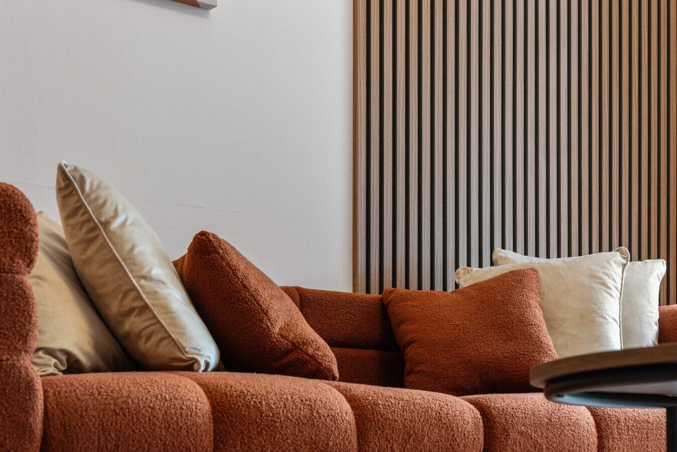 A sofa with multiple cushions in a room with a vertical striped wall.