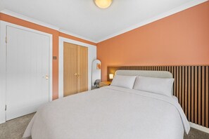 A hotel room with a large bed, a wooden wardrobe, a bedside table with a lamp, and a mirror on the wall.