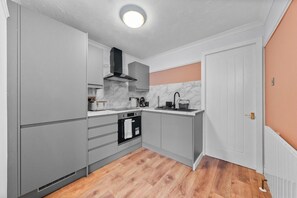 A compact kitchen with grey cabinets, a black oven, a marble backsplash, and a wooden floor.