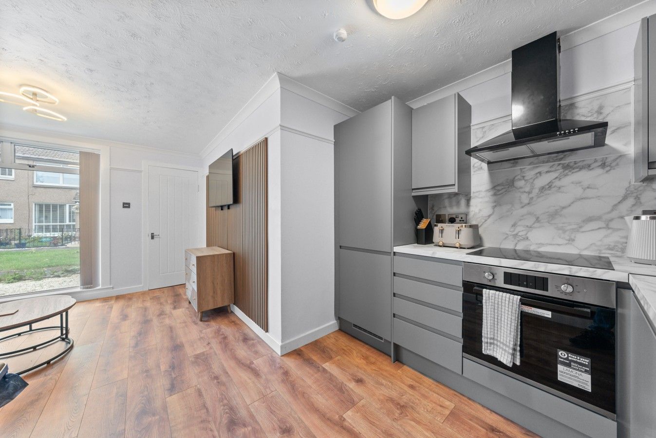 A modern kitchen with grey cabinetry, a black range hood, and a marble backsplash.