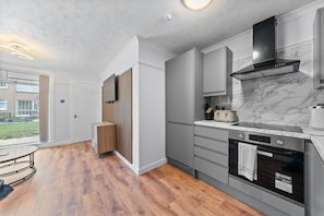 A modern kitchen with grey cabinetry, a black range hood, and a marble backsplash. - 2-bed Ground Floor Apartment with Free Parking Near Glasgow Airport (Renfrew)
