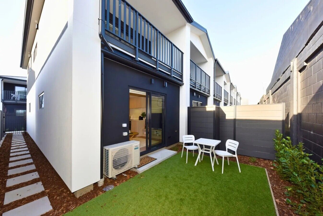 A modern residential building with a covered patio, a small lawn, and a white air conditioning unit.