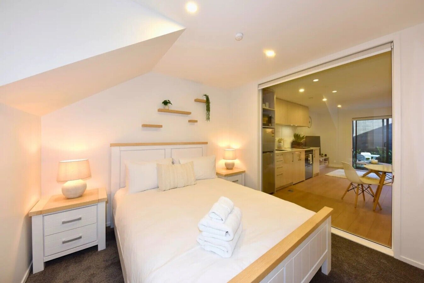 Ein Schlafzimmer mit Bett, Nachttischen und Blick auf eine Küche und einen Essbereich.
