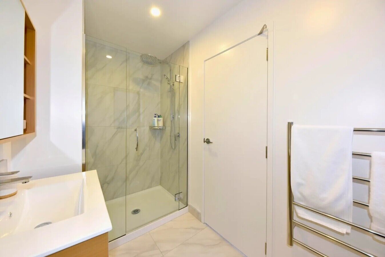 A modern bathroom with a glass-enclosed shower, a white sink, and a towel rack.
