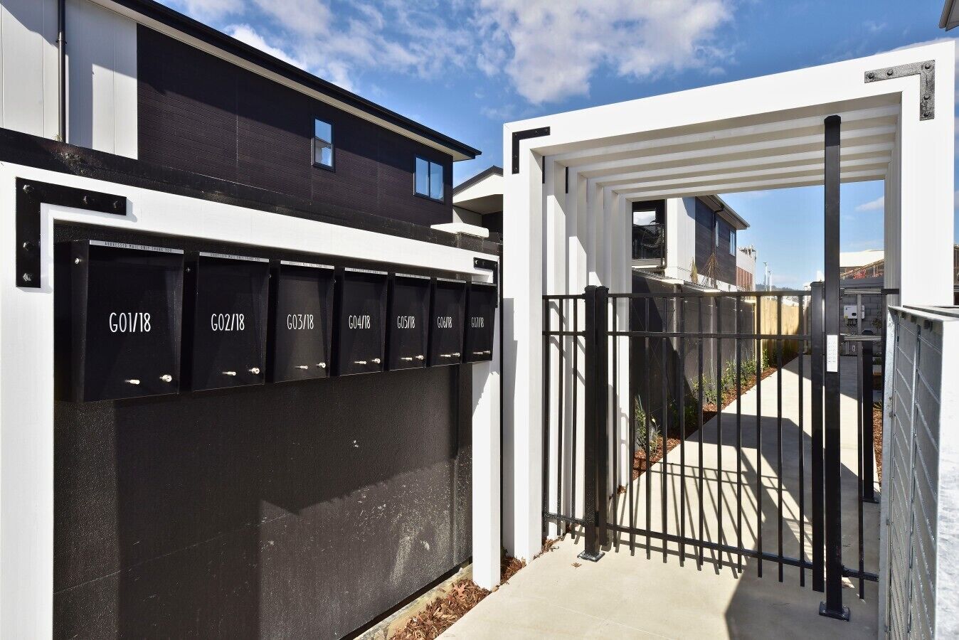 A gated entrance with numbered mailboxes, a clear sky, and a building with a dark facade and white trim.