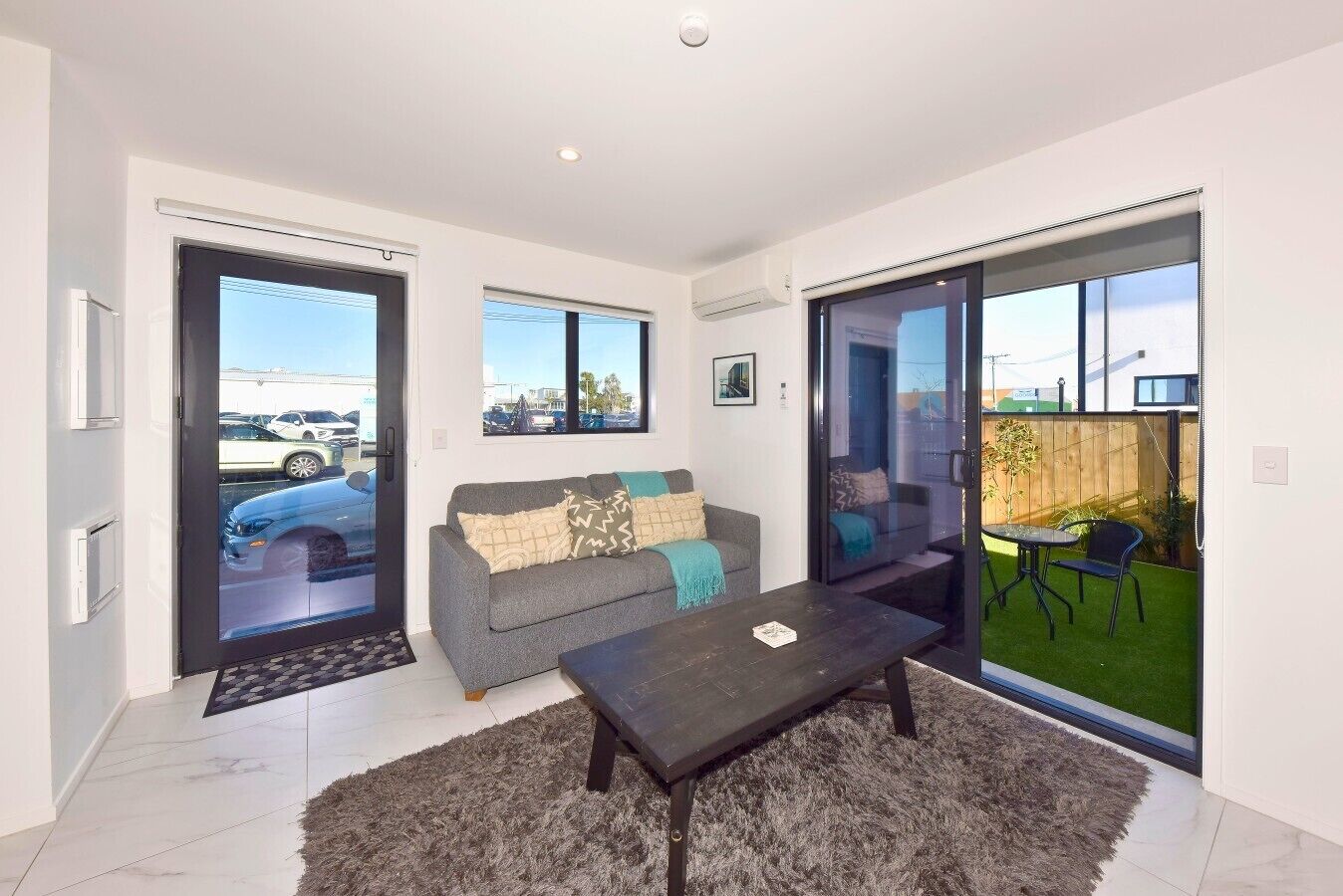 A modern living room with a sofa, a coffee table, and a sliding glass door leading to a patio with outdoor furniture.