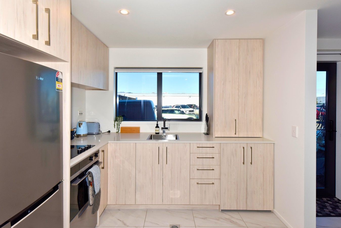A modern kitchen with a built-in oven, a sink, and a window with a view of a parking lot.