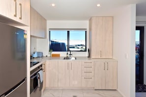 A modern kitchen with a built-in oven, a sink, and a window with a view of a parking lot. - The Modern Hideaway for Every Stay (Christchurch)