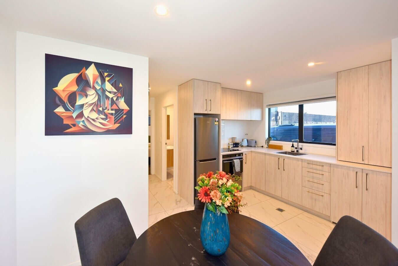 A modern kitchen with light wood cabinets, a stainless steel refrigerator, and a window providing a view of the outside.