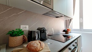 Une cuisine moderne avec un plan de travail en marbre, une miche de pain, une machine à café, un verre à vin et une fenêtre avec des rideaux.