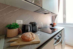 A modern kitchen with a marble countertop, a loaf of bread, a coffee maker, a wine glass, and a window with curtains. - Incanto 107 (Como)