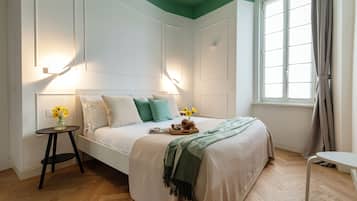 Un dormitorio con cama, mesitas de noche, ventana con cortinas y vistas al exterior.