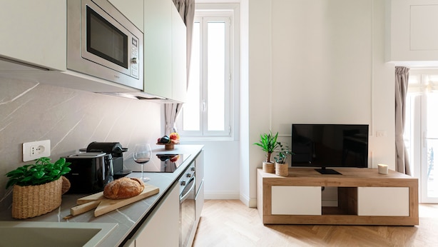 Une cuisine moderne équipée d’un four à micro-ondes, d’un grille-pain et d’une planche à découper en bois avec du pain. On y trouve également un téléviseur posé sur un meuble en bois et une plante en pot sur le comptoir.