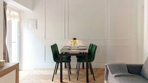 Un coin repas avec une table dressée pour quatre personnes, des chaises à revêtement vert et un canapé gris.