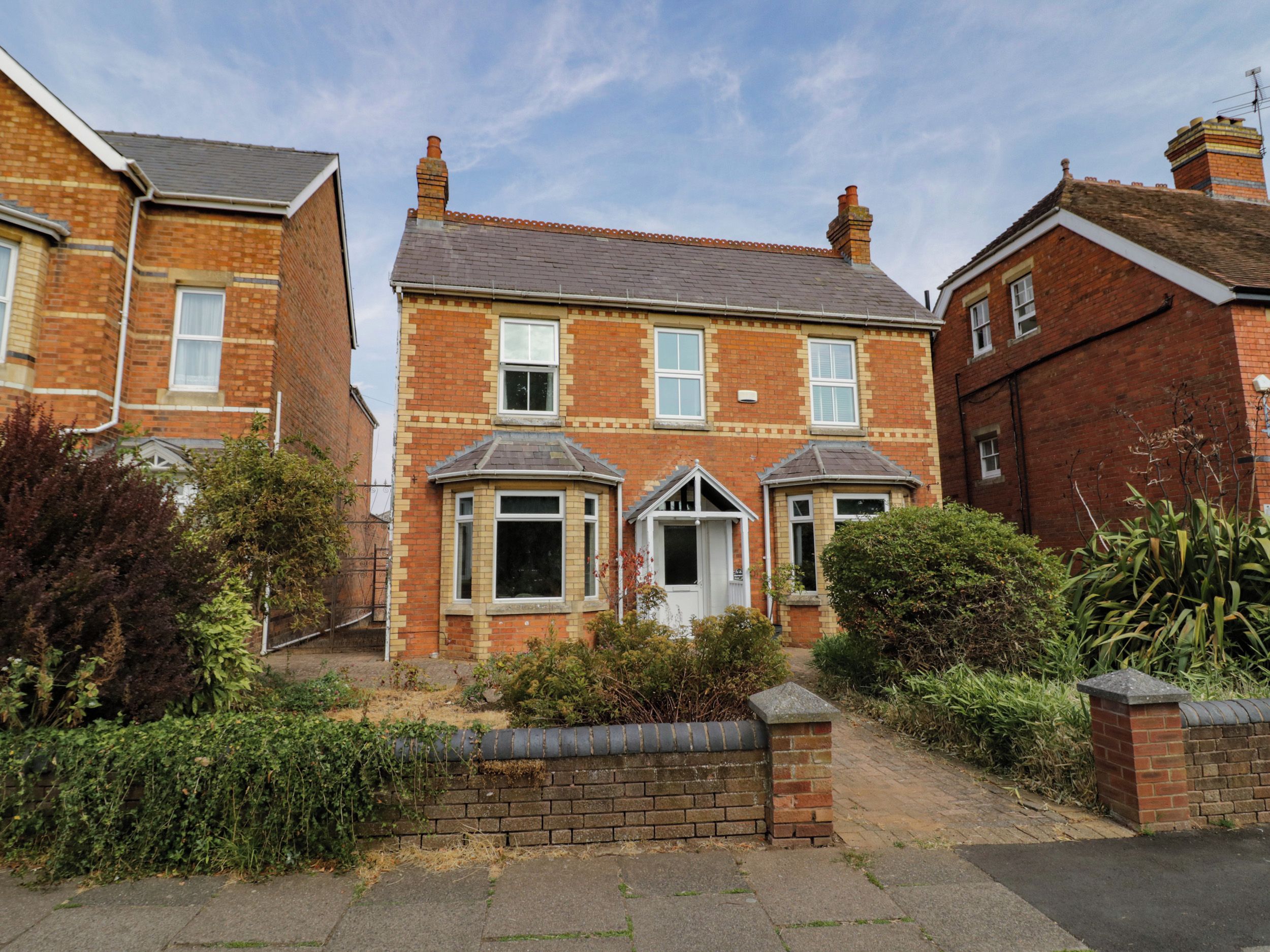 A two-story brick house with a front garden, a bay window, and a conservatory.