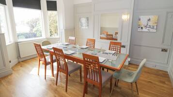 A dining room with a glass table, wooden chairs, and a view of the outdoors through large windows.