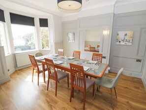 A dining room with a glass table, wooden chairs, and a view of the outdoors through large windows. - Astwood House (Malvern)