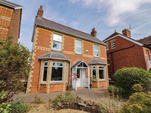 A two-story brick house with a front porch, a bay window, and a small garden area. - Astwood House (Malvern)