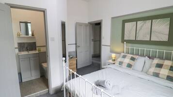 A bedroom with a bed, bedside table, and a nightstand. There is a bathroom with a sink and mirror. The room has a door leading to another room.