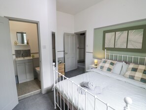 A bedroom with a bed, bedside table, and a nightstand. There is a bathroom with a sink and mirror. The room has a door leading to another room. - Astwood House (Malvern)