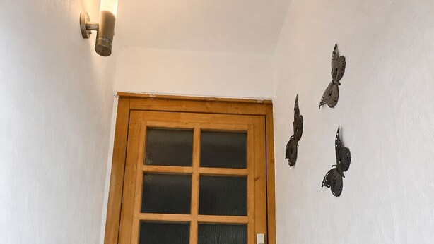 Eine Holztür mit Glasfenster, ein weißer Laternen und eine Fußmatte am Eingang.