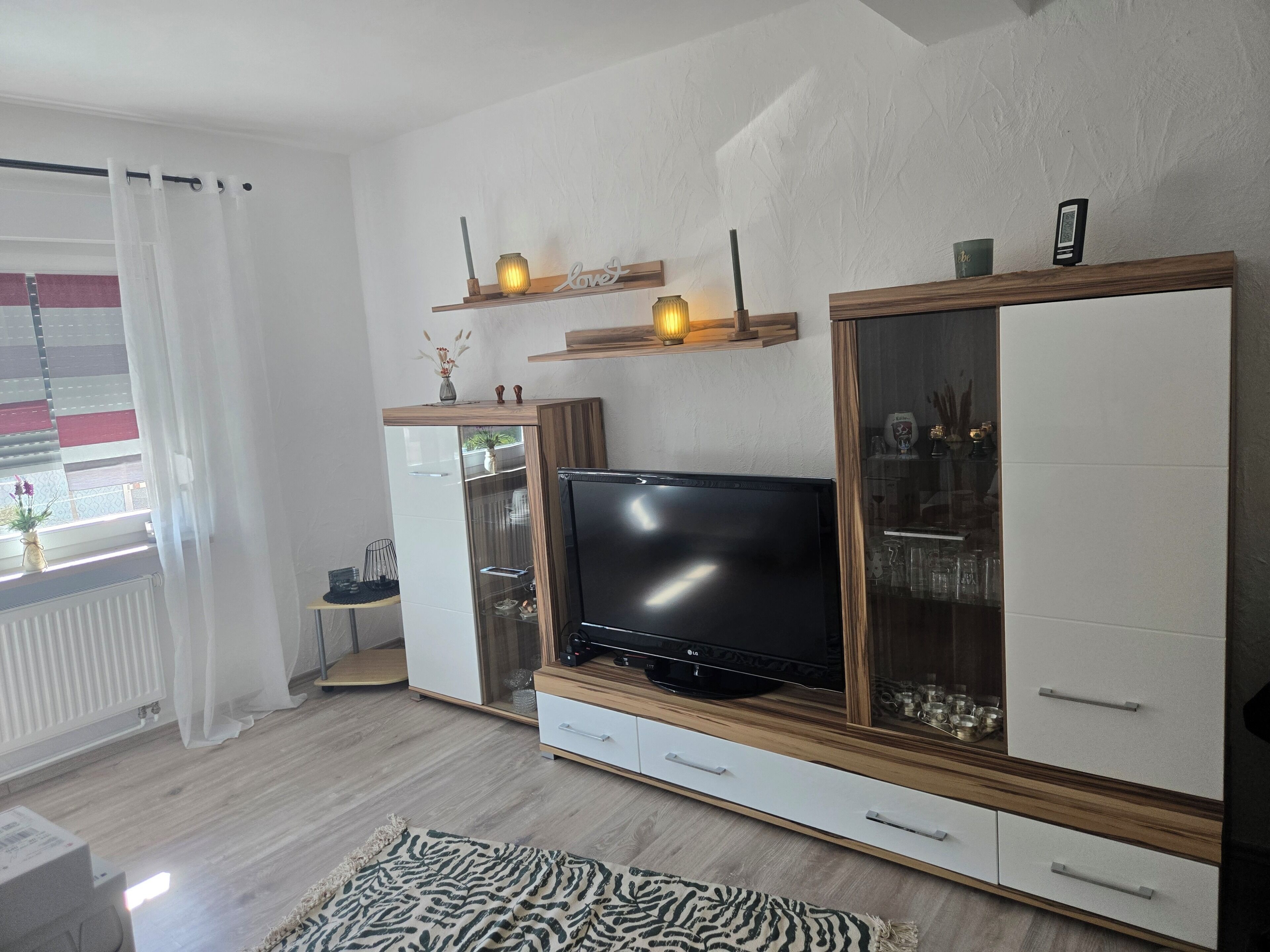 Ett modernt vardagsrum med en platt-TV, träskåp och ett skåp med glasluckor.