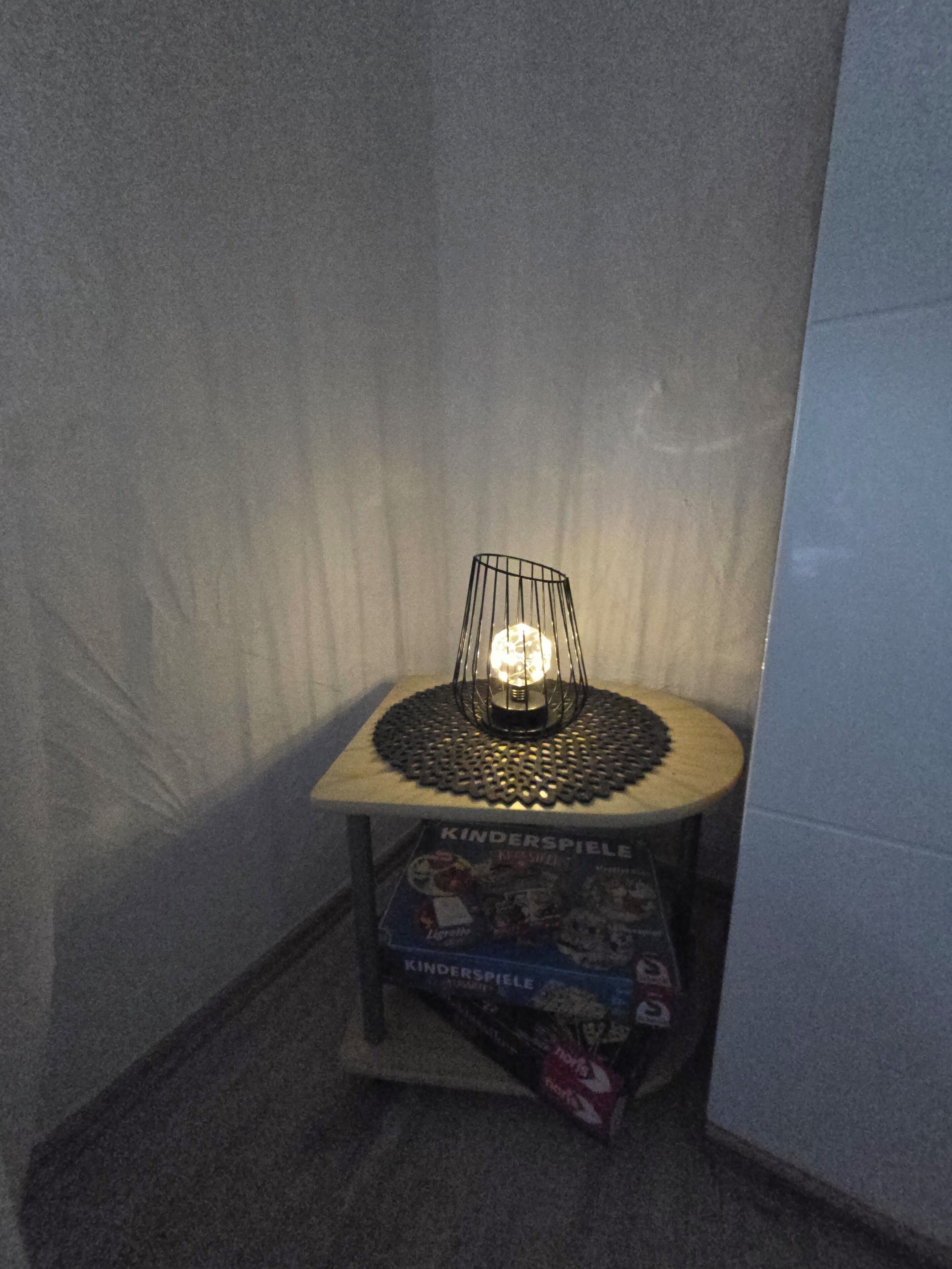 A corner of a room with a small table holding a decorative light fixture and a Kinder Spiele board game box.