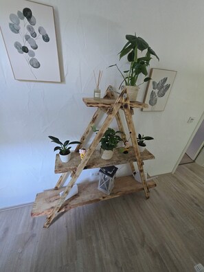 A wooden plant stand with multiple shelves holding potted plants and a decorative item.