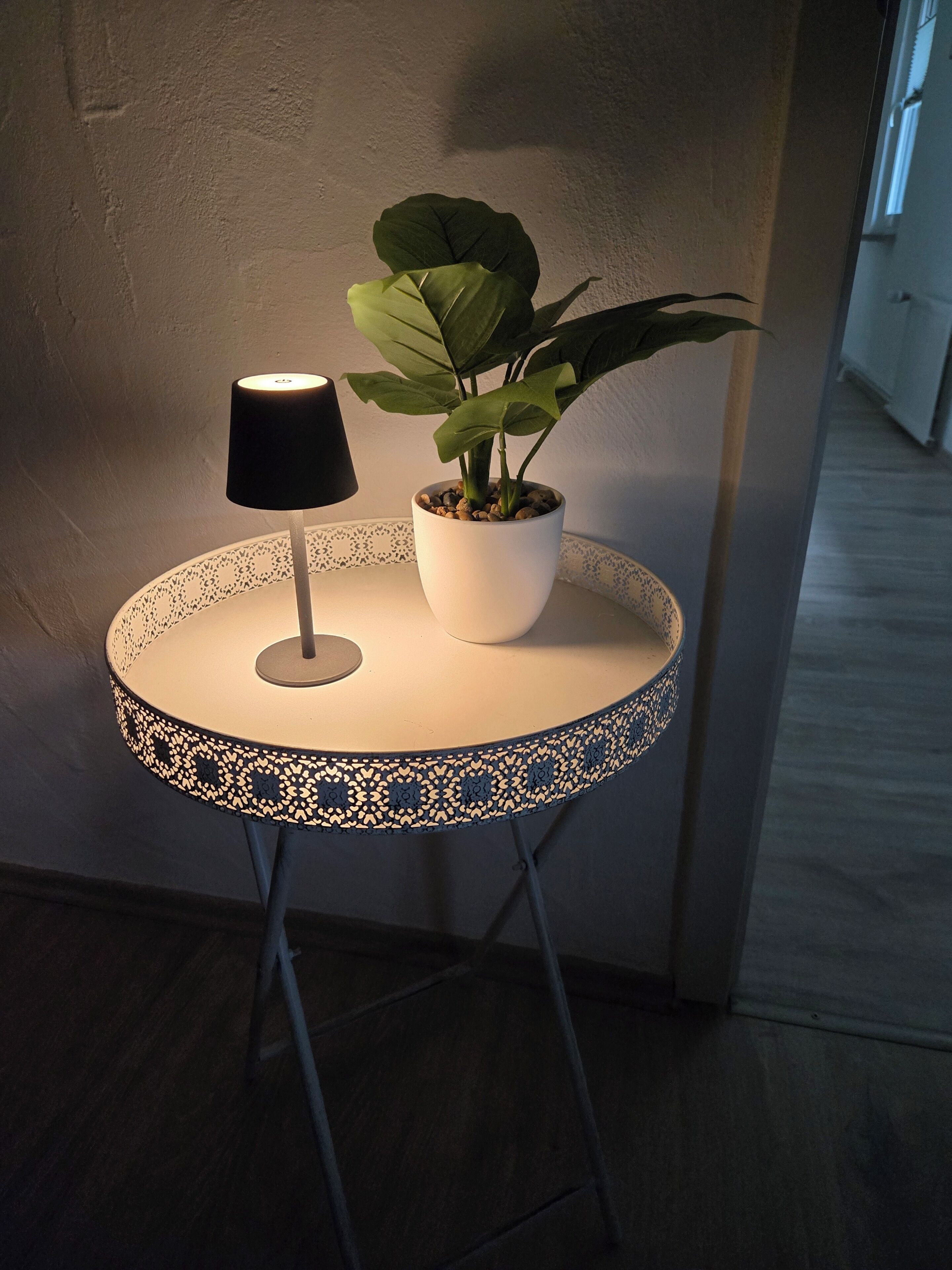 Een kleine ronde tafel met een lamp en een bloempot.