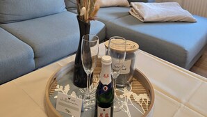 Ein Wohnzimmer mit grauem Sofa, einer Vase mit Trockenpflanzen, einem Tablett mit einer Weinflasche, Gläsern und einer Kerze.