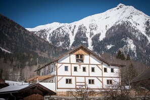 A traditional Alpine chalet with a symmetrical facade, multiple windows, and a prominent wooden gable. - Key to Heaven - Glacier Apartments (Flattach)