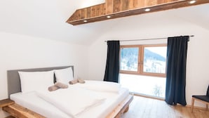 Ein Schlafzimmer mit einem hölzernen Bettgestell, einem großen Fenster mit Vorhängen und Blick auf eine verschneite Landschaft.