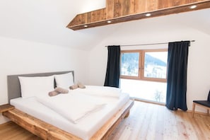 Un dormitorio con estructura de cama de madera, un ventanal con cortinas y vista a un paisaje nevado.