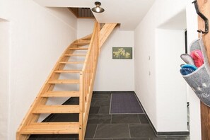 A wooden staircase leading to a landing with a dark tiled floor, a small mat, and a wall-mounted hook with items. - Key to Heaven - Glacier Apartments (Flattach)