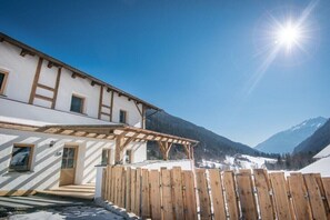 A building with a wooden deck and a wooden fence, surrounded by snow-covered mountains. - Key to Heaven - Glacier Apartments (Flattach)