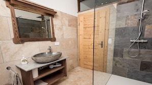 Ein Badezimmer mit einem Steinkonstruktion Waschbecken, einem hölzernen Waschtisch, einer Duschkabine aus Glas und einer Holztür.