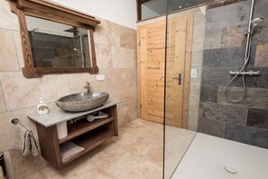 Un baño con lavamanos de piedra, tocador de madera, cabina de ducha de vidrio y puerta de madera.