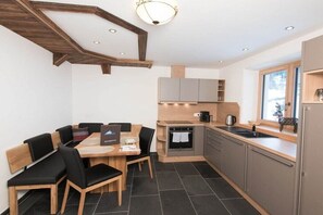 A modern kitchen with a dining area, featuring a wooden ceiling, built-in cabinets, and a window with a view. - Key to Heaven - Glacier Apartments (Flattach)