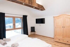 A bedroom with a bed, a TV mounted on the wall, a wooden wardrobe, and a window with curtains. - Key to Heaven - Glacier Apartments (Flattach)