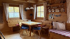 Et interiør af en træhytte med et spisebord, stole, en bænk og en sofa.