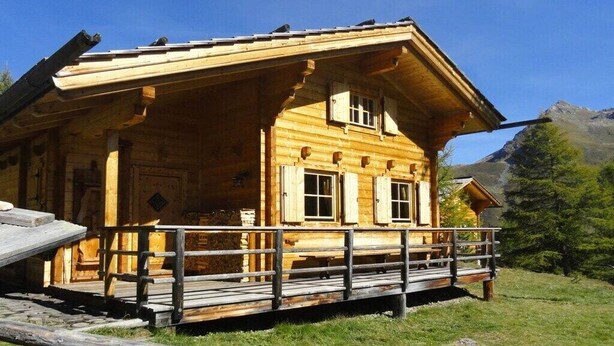 En træhytte med veranda, et lille vindue og et bjerg i baggrunden.