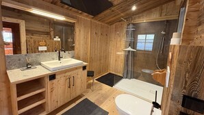 Et badeværelse i en træhytte med vask, spejl, brusebad og toilet.