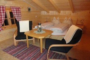 A cozy wooden cabin room with a bed, a table, two chairs, and a window with curtains. - Alpine hut in Mörtschach with barbecue (Mörtschach)