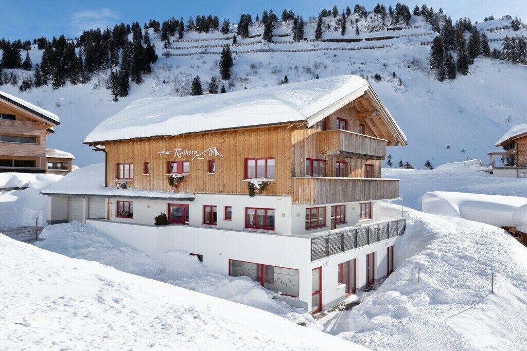 Un immeuble en bois à plusieurs étages, avec une piste de ski en arrière-plan.