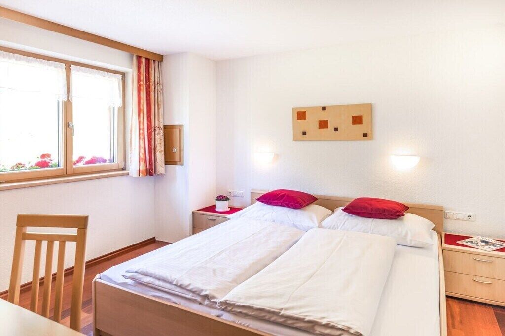 Habitació d'hotel amb un llit, una cadira, una taula de nit, una finestra amb cortines i una obra d'art penjada a la paret.