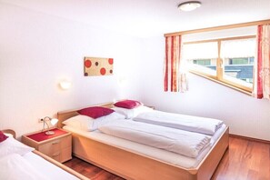 Ein Doppelbett mit zwei Kissen, ein Nachttisch mit Lampe, eine Wanduhr und ein Fenster mit Vorhängen.