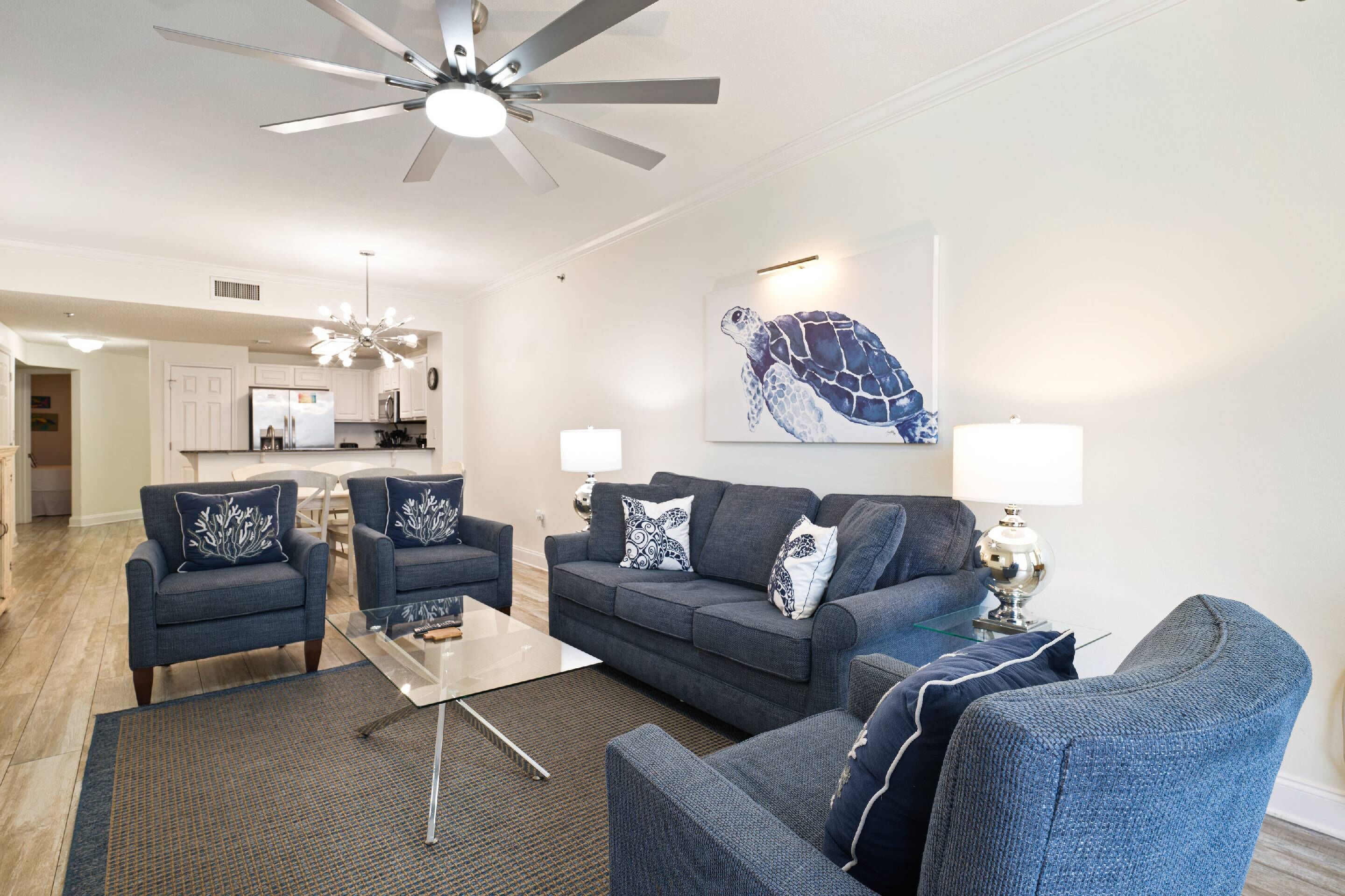 A modern living room with a ceiling fan, a large wall mural of a sea turtle, and a kitchen in the background.