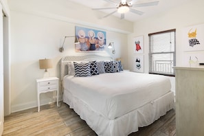 A bedroom with a large bed, a nightstand, a lamp, a ceiling fan, and artwork on the walls. - New Gulf-Front Listing| Amazing Views| Pools| Tennis Courts| Gym| Free Rounds of Golf (Pensacola)